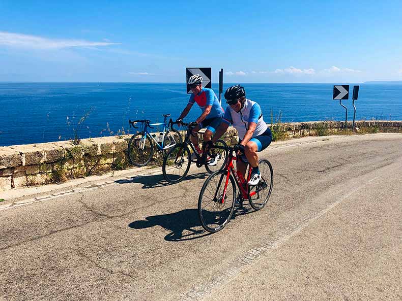 Two cyclists riding near the Southern Italian sea