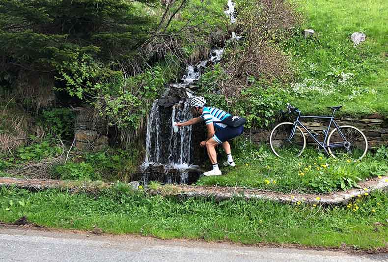 a cyclist filling his water bottle from a cascading mountain stream by the road