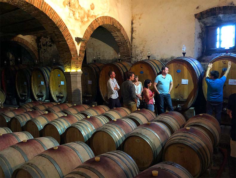 A group of people in a barrel filled room during a Tuscan wine tour