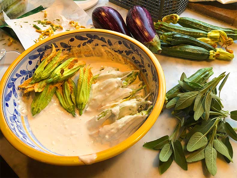 Eggplants zucchinis, and zucchini flowers in a bowl of batter