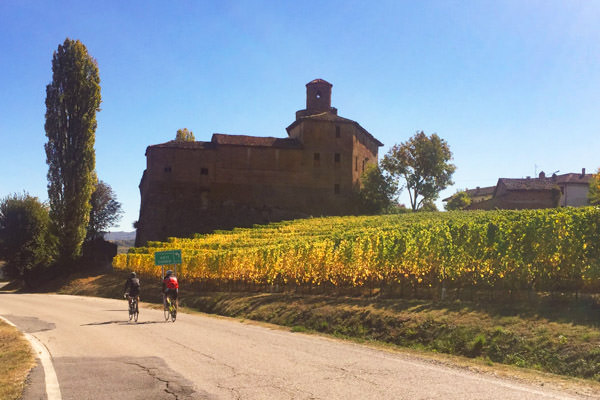 two riders cycling past an old castle near La Morra