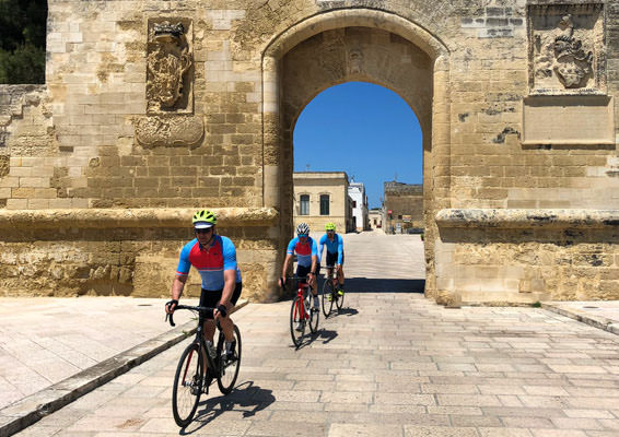 Three riders under a stone arch in Puglia