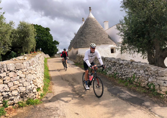 Two riders cycling past the iconic trulli in Puglia