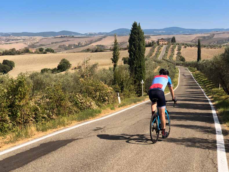 A cyclist on a road through the iconic Tuscany landscape